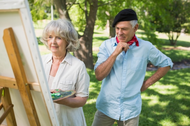 Homme regardant la femme mûre peindre dans le parc