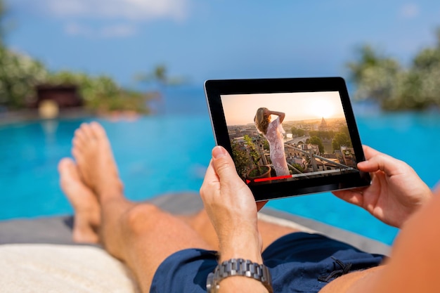 Homme regardant un film sur une tablette au bord de la piscine