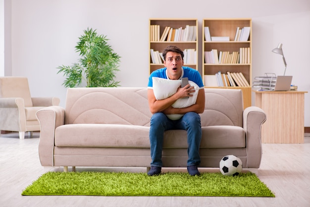 Homme regardant le football à la maison assis sur un canapé