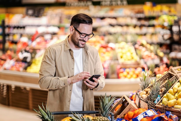 Un homme regardant la liste de courses au téléphone et achetant au supermarché