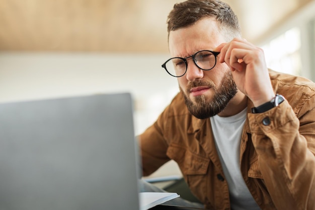 Homme regardant un ordinateur portable plissant les yeux portant des lunettes à l'intérieur