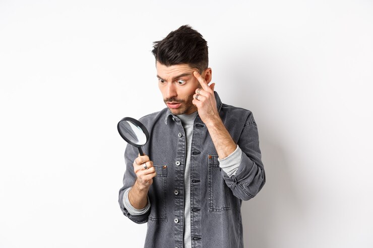 Photo homme regardant à travers la loupe et étirant la paupière pour voir clairement, debout sur fond blanc.