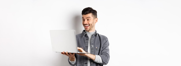 Homme regardant une vidéo drôle sur un ordinateur portable en riant de l'écran de l'ordinateur et souriant joyeux debout sur blanc