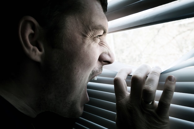 Un homme regarde par la fenêtre ouvrant les stores