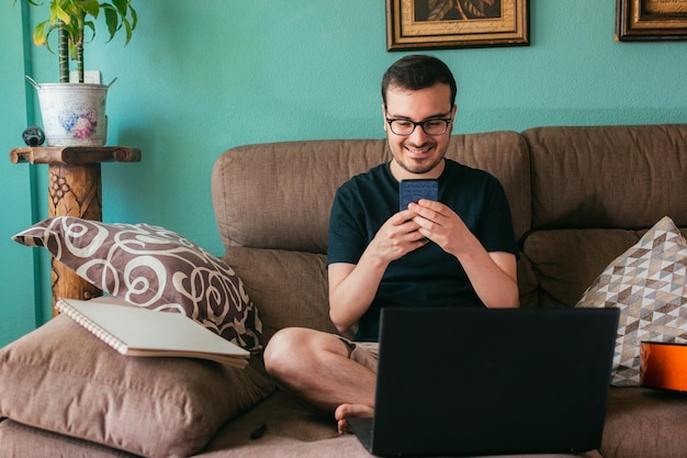 L'homme regarde son téléphone portable à la maison assis sur un canapé