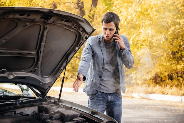 Un homme regarde sous le capot ouvert d'une voiture La voiture est tombée en panne sur la route Le moteur fume