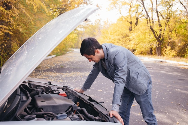 Un homme regarde sous le quota d'une voiture cassée