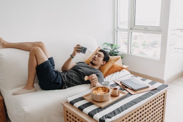 Un homme regarde la télévision en ligne et mange une collation au lieu de travailler à domicile