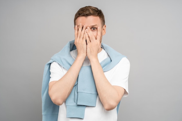 Photo l'homme regarde à travers les doigts effrayé homme d'âge moyen couvre le visage avec les mains vue effrayante effrayante