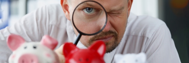 L'homme regarde à travers une loupe à la tirelire