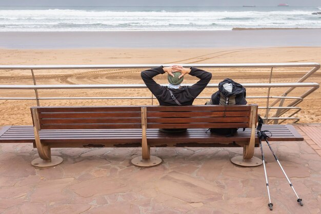 Homme relaxant sur un banc sur la côte de l'océan Atlantique Touriste avec sac à dos sur la plage Pèlerin au repos