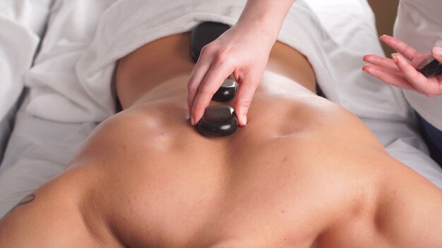 Homme relaxant dans le centre de bien-être avec des pierres chaudes sur le corps.