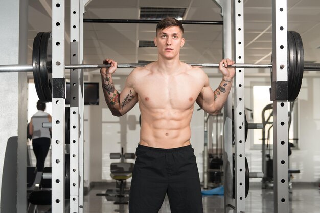 Homme de remise en forme à l'aide d'haltères exerçant des jambes à l'intérieur de la salle de sport