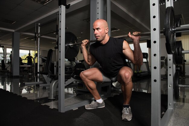 Homme de remise en forme à l'aide d'haltères exerçant des jambes à l'intérieur de la salle de sport