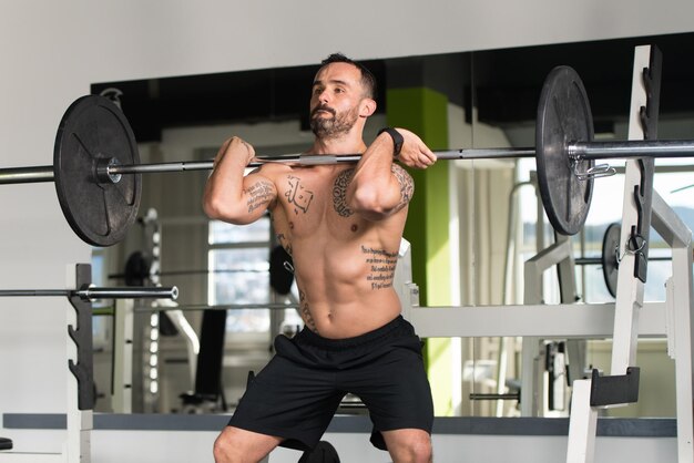 Homme de remise en forme en bonne santé travaillant sur les jambes avec des haltères dans un exercice de squat avant de salle de sport