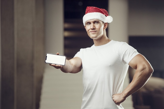 Homme de remise en forme en costume de chapeau de père Noël dans une salle de sport avec téléphone portable
