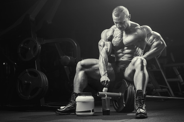 Homme de remise en forme à l'entraînement dans une salle de sport avec pot de poudre de protéines. Concept de musculation