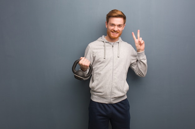 Homme de remise en forme jeune rousse amusant et heureux faisant un geste de victoire. Tenant un haltère.