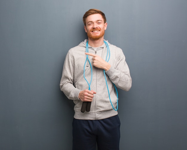 Homme de remise en forme jeune rousse pointant sur le côté avec le doigt. Il tient une corde à sauter.