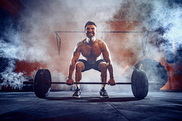 Homme de remise en forme musculaire faisant deadlift une barre au-dessus de sa tête dans un centre de remise en forme moderne. Entraînement fonctionnel. Exercice Snatch. Fumée sur le mur.