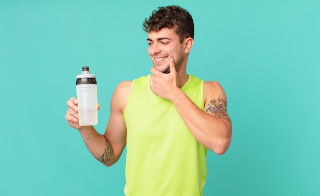 Homme de remise en forme souriant avec une expression heureuse et confiante avec la main sur le menton, se demandant et regardant sur le côté