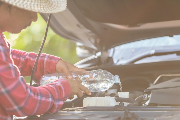 L'homme remplit l'eau du réservoir du radiateur de la voiture et vérifie le moteur avant de commencer le voyage Entretien de la voiture ou concept de vérification