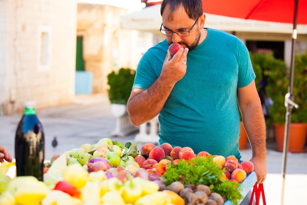 Homme reniflant la pêche au marché en plein air. Fruits et légumes d'été, aliments frais