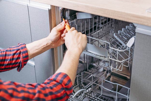 Homme réparant un lave-vaisselle. Main masculine avec tournevis installe les appareils de cuisine