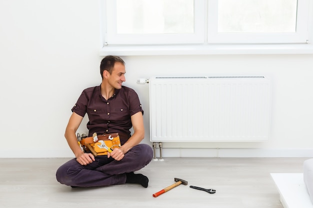 L'homme Répare La Batterie Du Radiateur Dans La Pièce. Travaux De Réparation D'entretien Rénovation Dans L'appartement. Restauration Du Chauffage. Clé En Mains