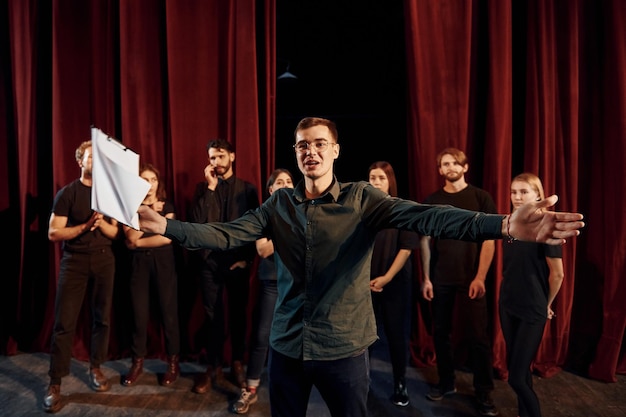 Un homme répète son rôle un groupe d'acteurs en vêtements de couleur foncée à la répétition au théâtre