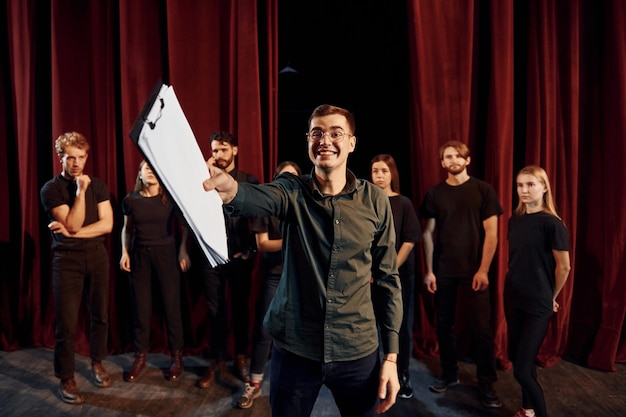 Un homme répète son rôle un groupe d'acteurs en vêtements de couleur foncée à la répétition au théâtre