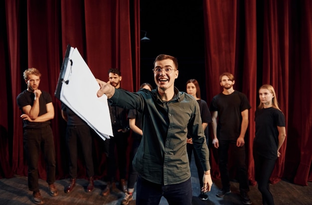 Un homme répète son rôle un groupe d'acteurs en vêtements de couleur foncée à la répétition au théâtre