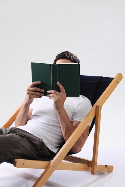 Homme reposant sur la chaise longue tenant un livre sur fond blanc