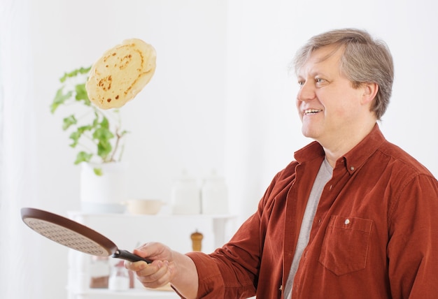 L'homme retourne la crêpe dans l'air dans la cuisine