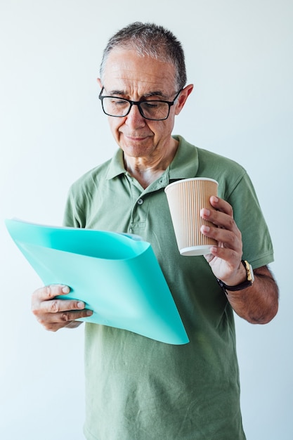 Homme à la retraite entrepreneur vêtu d'une chemise verte et des lunettes, tenant un dossier avec un rapport et un café