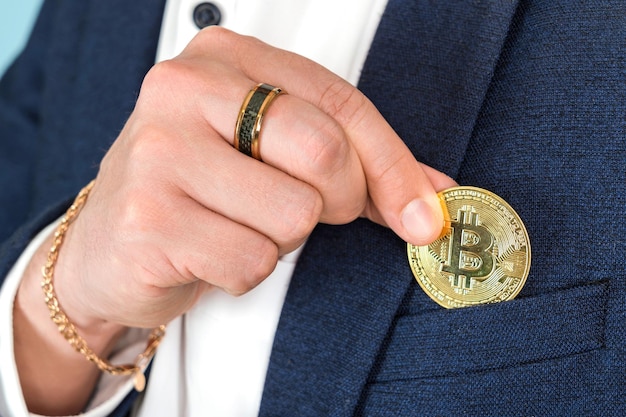 Un homme riche met une pièce d'or bitcoin dans la poche de poitrine de sa veste, gros plan