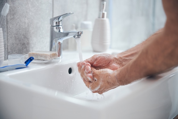 homme rinçant le savon de ses mains dans la salle de bain