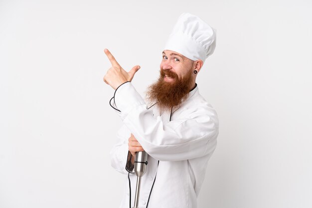 Homme rousse à l'aide d'un mélangeur à main sur un mur blanc isolé pointant avec l'index une excellente idée