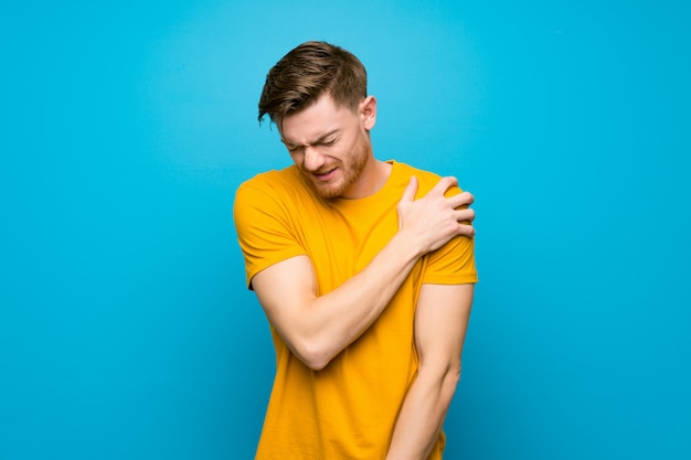 Homme rousse au mur bleu souffrant de douleur à l'épaule pour avoir fait un effort