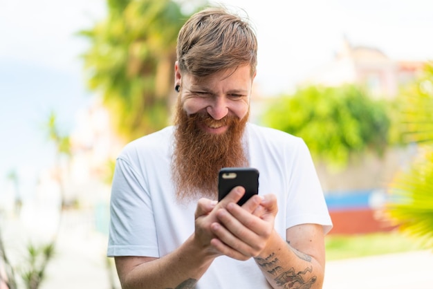 Homme rousse avec barbe envoyant un message ou un e-mail avec le mobile