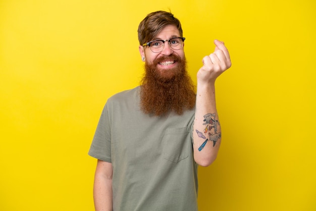 Homme rousse avec barbe isolé sur fond jaune faisant un geste d'argent