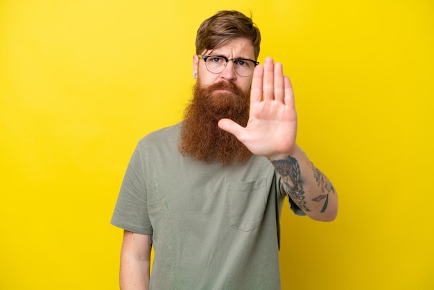 Homme rousse avec barbe isolé sur fond jaune faisant un geste d'arrêt