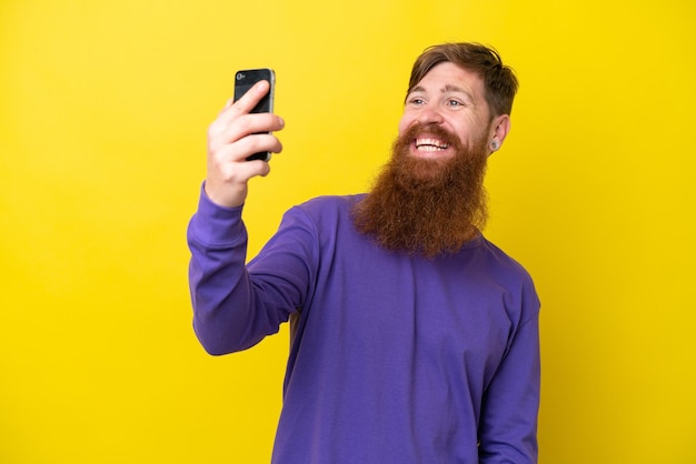 Homme rousse avec barbe isolé sur fond jaune faisant un selfie