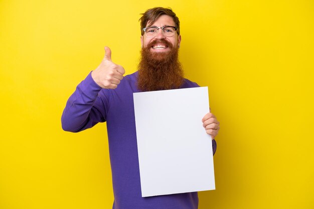 Homme rousse avec barbe isolé sur fond jaune tenant une pancarte vide avec le pouce vers le haut