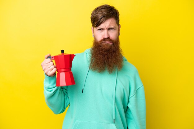 Homme rousse avec barbe tenant une cafetière isolée sur fond jaune avec une expression triste