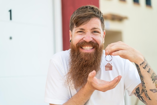 Homme rousse avec barbe tenant les clés de la maison avec une expression heureuse