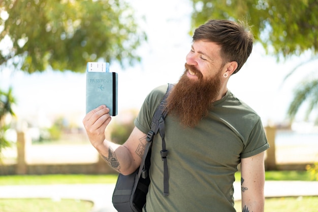 Homme rousse avec barbe tenant un passeport à l'extérieur avec une expression heureuse