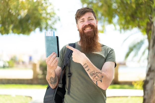 Homme rousse avec barbe tenant un passeport à l'extérieur et le pointant