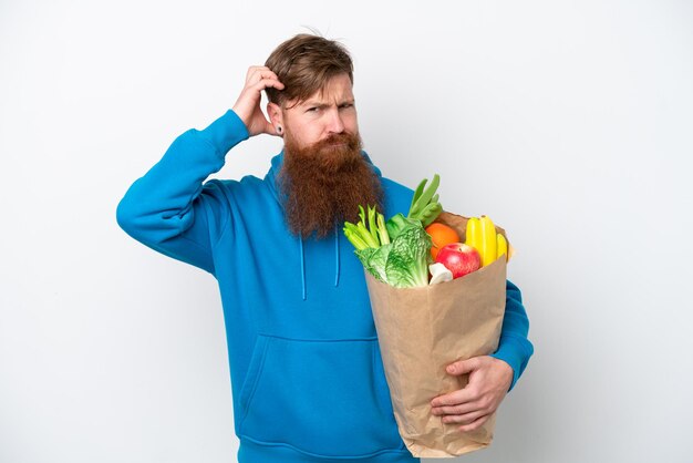 Homme rousse avec barbe tenant un sac d'épicerie isolé sur fond blanc ayant des doutes