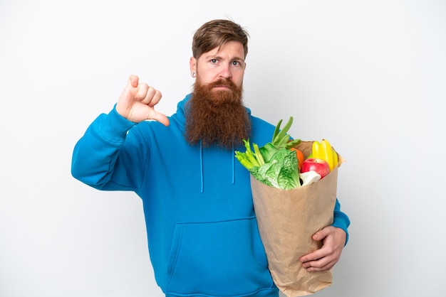 Homme rousse avec barbe tenant un sac d'épicerie isolé sur fond blanc montrant le pouce vers le bas avec une expression négative